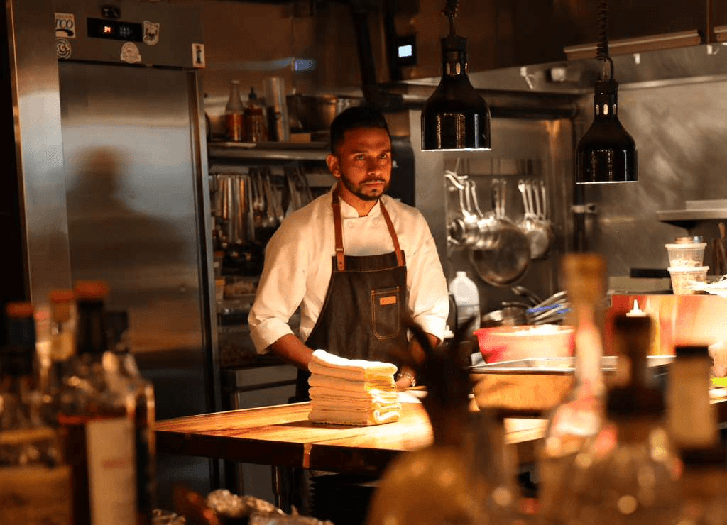 Chef Reshan Koralage in chef whites and apron behind a butcher block in a professional kitchen